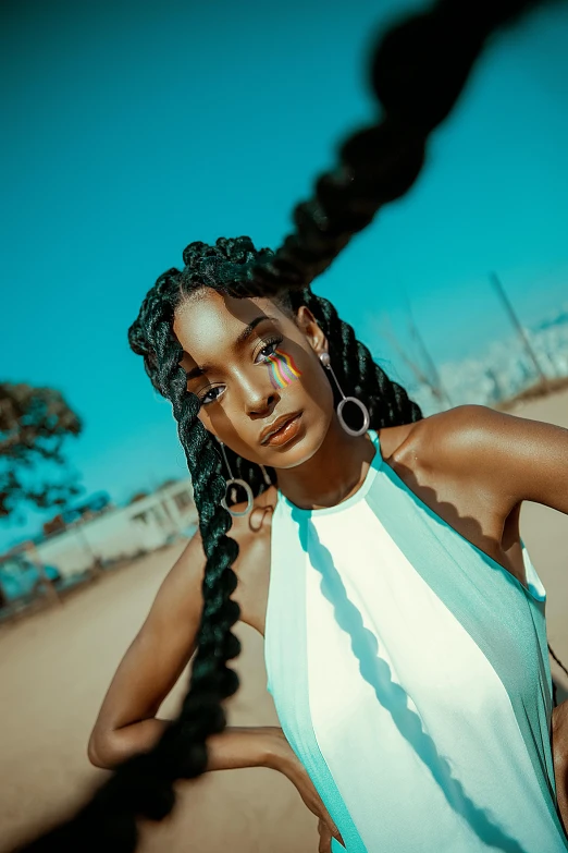 a woman standing on top of a sandy beach, an album cover, trending on pexels, afrofuturism, hair blue two long braids, blue symmetric eyes 24yo, 5 0 0 px models, hollywood promotional image