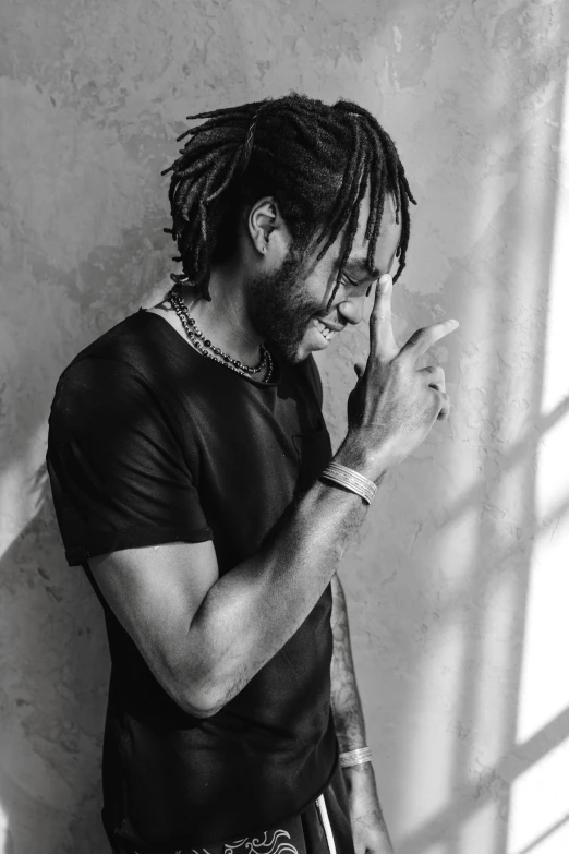 a man with dreadlocks standing in front of a wall, a black and white photo, trending on pexels, childish gambino, next to a big window, with index finger, profile picture