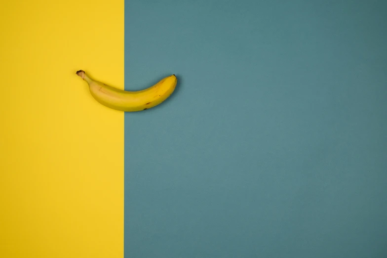 a banana sitting on top of a yellow and blue wall, half and half, teal studio backdrop, on grey background, a brightly coloured