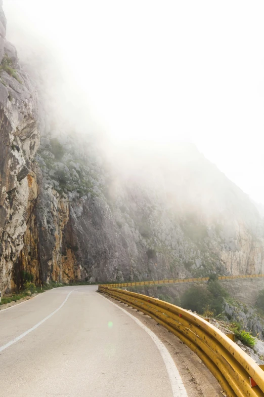 a car driving down a mountain road on a foggy day, boka, sheer cliffs surround the scene, yellow, limestone