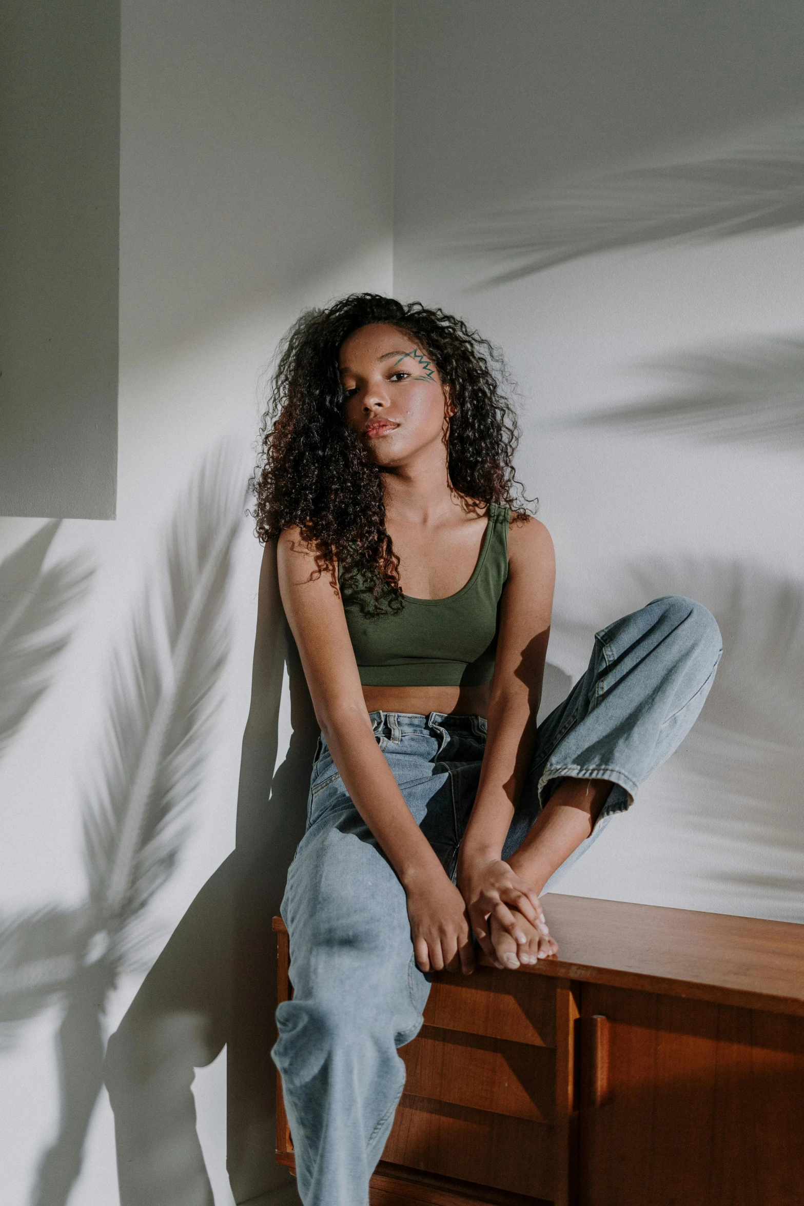 a woman sitting on top of a wooden table, trending on pexels, renaissance, casual green clothing, she has olive brown skin, croptop, standing in corner of room