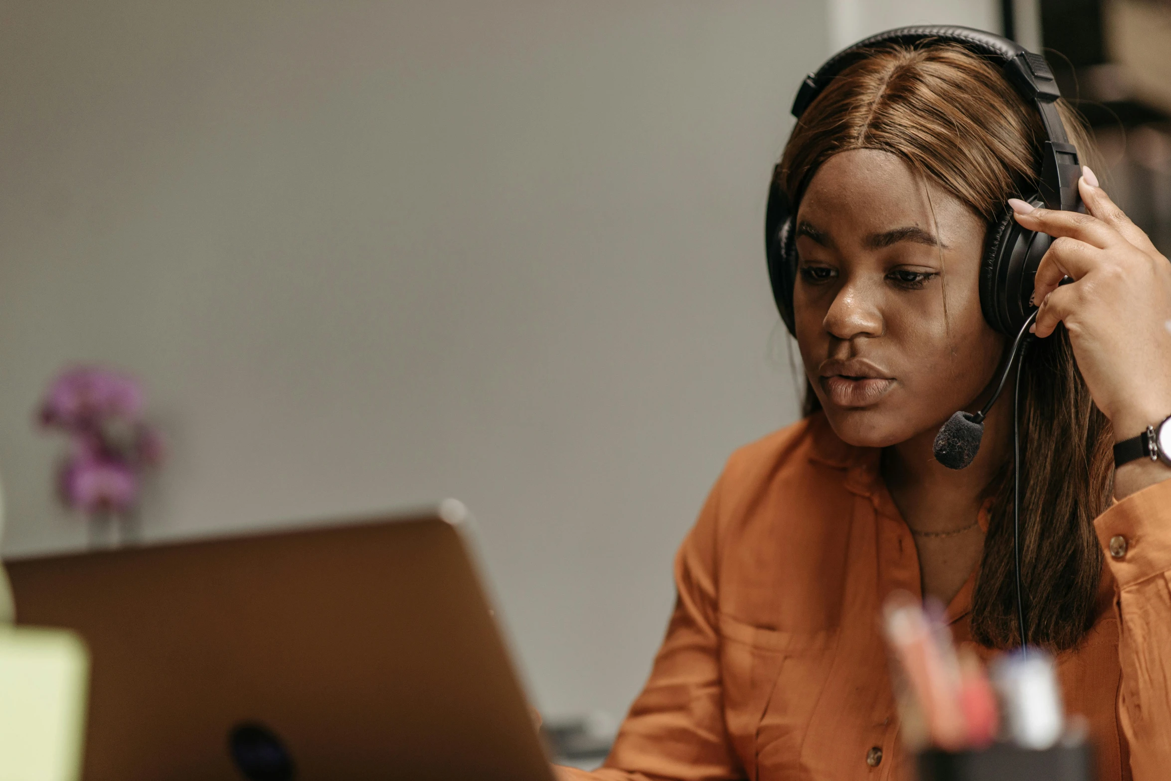 a woman sitting in front of a laptop wearing headphones, trending on pexels, renaissance, teaching, orange halo around her head, african woman, professional photo