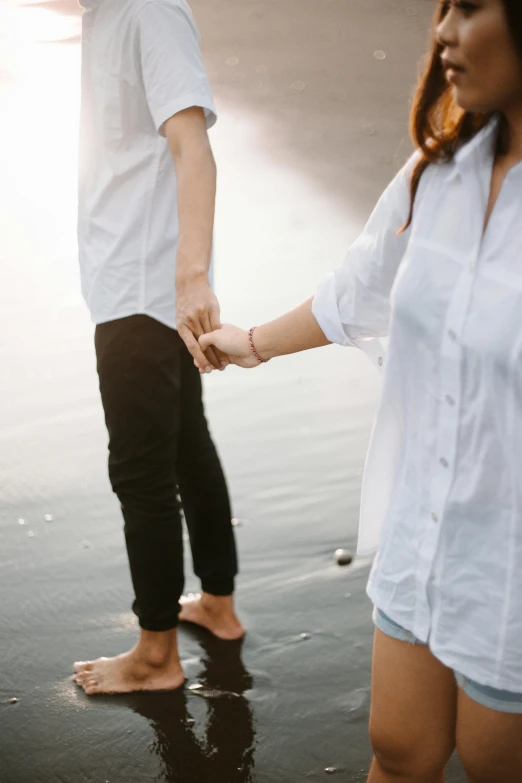 a man and a woman holding hands on a beach, a picture, trending on unsplash, wearing a light shirt, on grey background, romantic lead, teasing