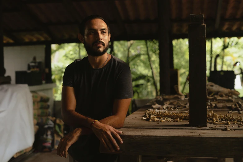 a man sitting on top of a wooden table, a portrait, pexels contest winner, in a jungle environment, portrait of danny gonzalez, in a workshop, profile image