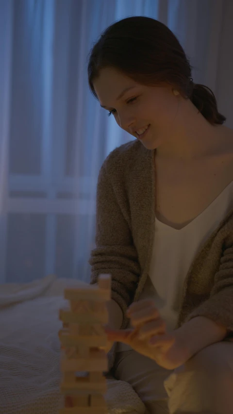 a woman sitting on a bed playing with blocks, by Eero Järnefelt, pexels contest winner, night time footage, soft light.4k, serene smile, cinematic pastel lighting