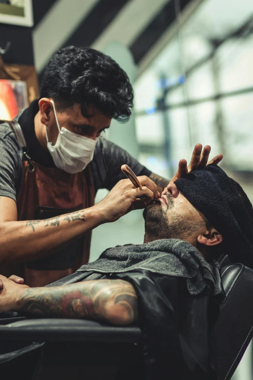 a man getting his hair cut by a barber, a tattoo, pexels contest winner, surgical mask covering mouth, thumbnail, malaysian, rugged textured face