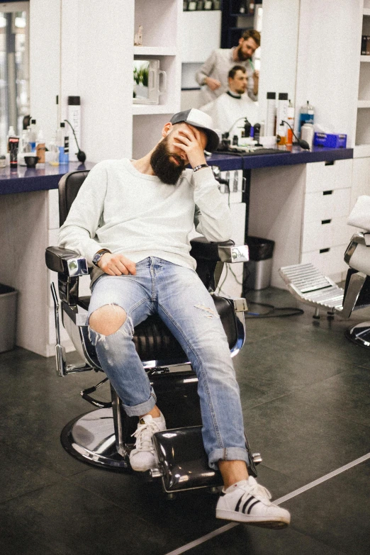 a man sitting in a chair in a barber shop, trending on pexels, happening, ripped jeans, sad face, bearded, really long