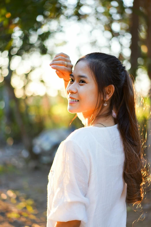 a woman that is standing in the dirt, light smile, in the morning light, with a ponytail, south east asian with round face