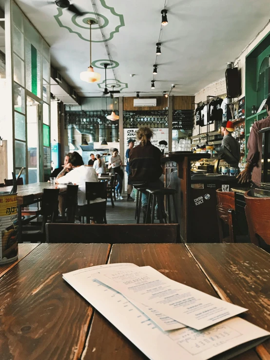 a menu sitting on top of a wooden table, a photo, by Niko Henrichon, pexels contest winner, happening, tel aviv street, interior of a small, aussie baristas, seen from the back