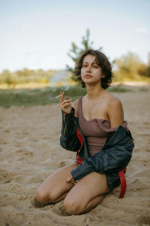 a woman sitting in the sand smoking a cigarette, by Attila Meszlenyi, trending on pexels, fine art, cute girl wearing tank suit, wearing a leather jacket, androgynous person, ukrainian girl