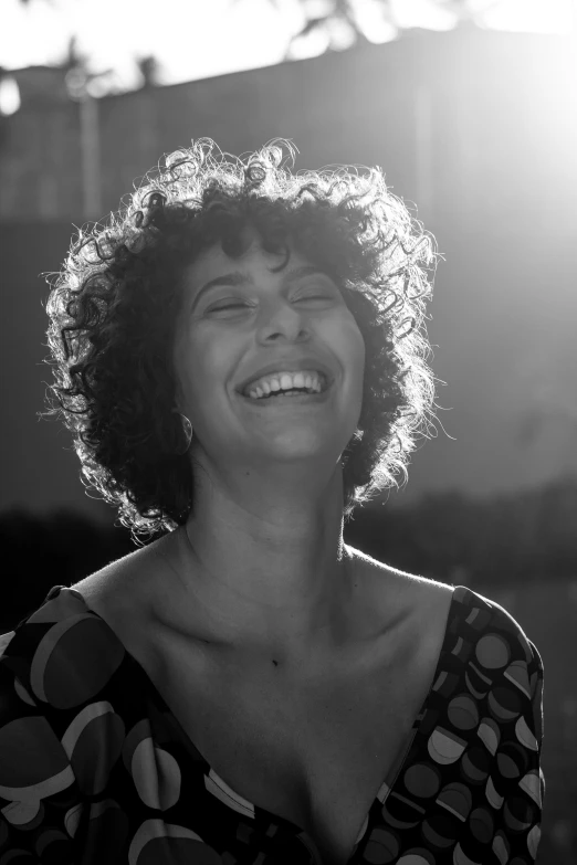 a black and white photo of a woman laughing, by Giovanni Pelliccioli, short black curly hair, with the sun shining on it, eytan zana, smiling at camera