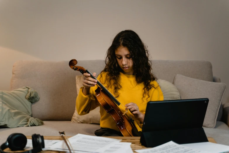 a woman sitting on a couch playing a violin, pexels contest winner, wearing a yellow hoodie, avatar image, studying, professional image