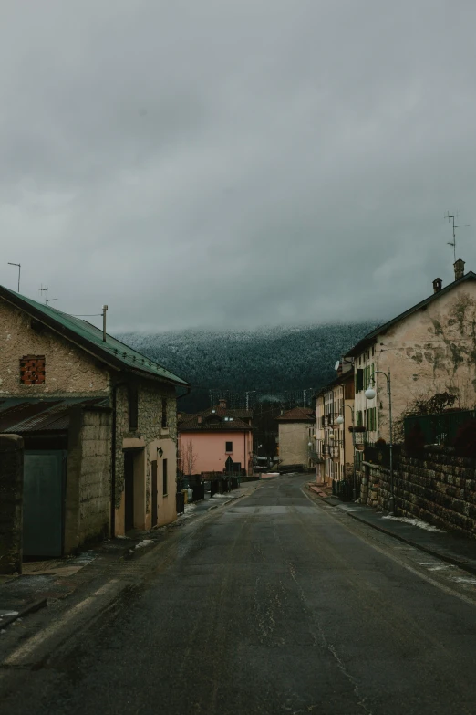 an empty street with buildings and mountains in the background, a picture, les nabis, gloomy colors, french village exterior, snowy apennines, dark and gritty