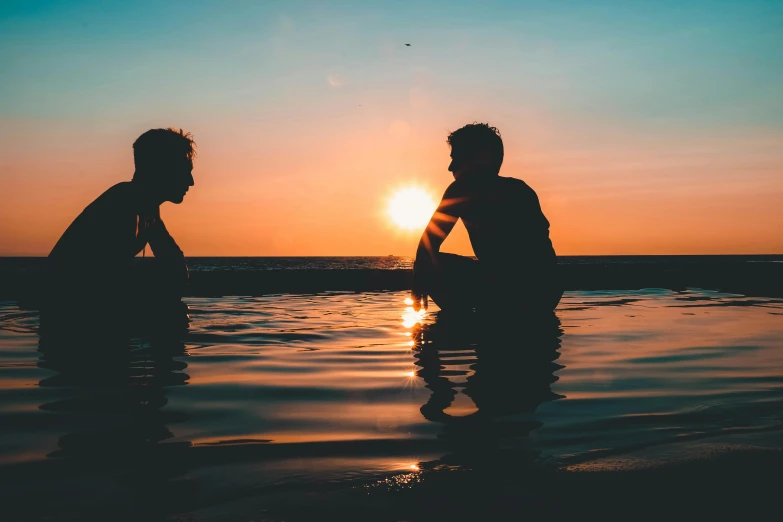 two men sitting in the water at sunset, pexels contest winner, brunette boy and redhead boy, talking, ((sunset)), good friends