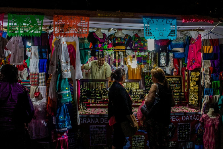 a group of people standing in front of a store, by Alejandro Obregón, pexels contest winner, colorful robes, underlit, some stalls, mayan