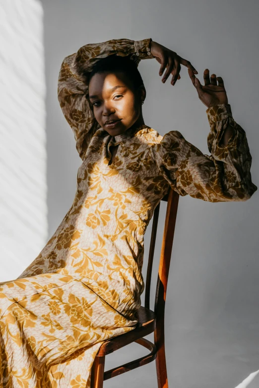 a woman sitting on top of a wooden chair, by Winona Nelson, trending on pexels, baroque, yellow ornate dress, brown skinned, delicate patterned, puff sleeves