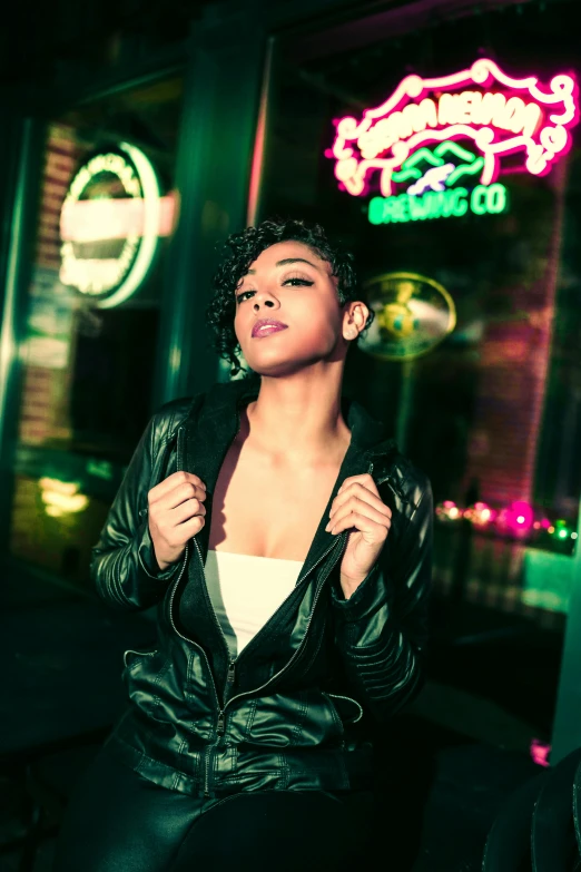 a woman in a leather jacket standing in front of a neon sign, curly and short top hair, high - key lighting, olive skinned, r&b
