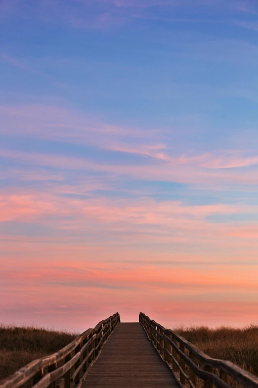 a wooden walkway leading to the beach at sunset, by Peter Churcher, romanticism, rock arches, pink landscape, pembrokeshire, large twin sunset