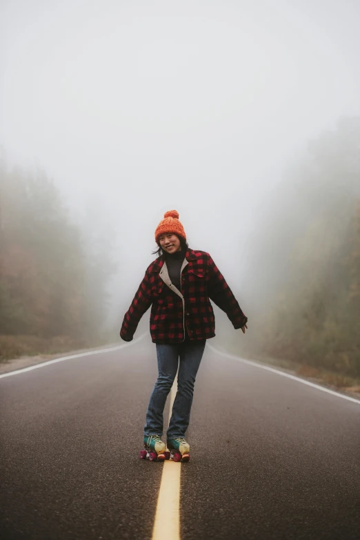 a woman riding a skateboard down a foggy road, a picture, pexels contest winner, she is smiling and excited, flannel, hiking clothes, cold weather