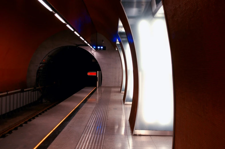 a train traveling down a train track next to a tunnel, by Jens Søndergaard, unsplash, art nouveau, brutalist futuristic interior, blue and red lights, dark city bus stop, chilean