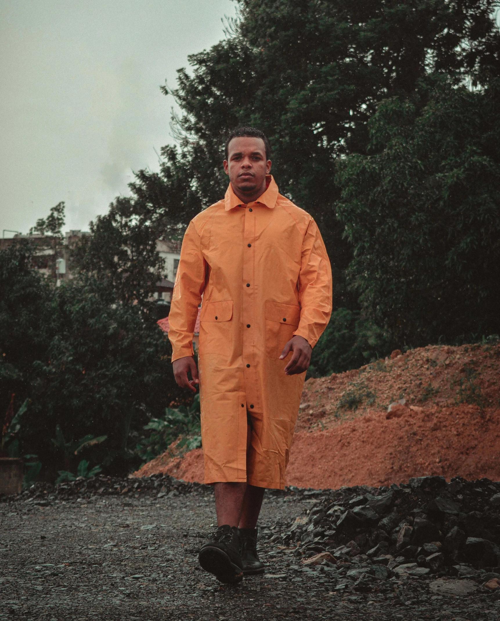 a man in an orange raincoat walking down a dirt road, an album cover, unsplash, realism, puerto rico, he is wearing a trenchcoat, yellow overall, pose 4 of 1 6