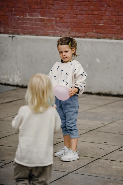 a little girl standing next to a little girl holding a frisbee, by Anita Malfatti, pexels contest winner, wearing casual clothing, balloon, urban surroundings, promotional image