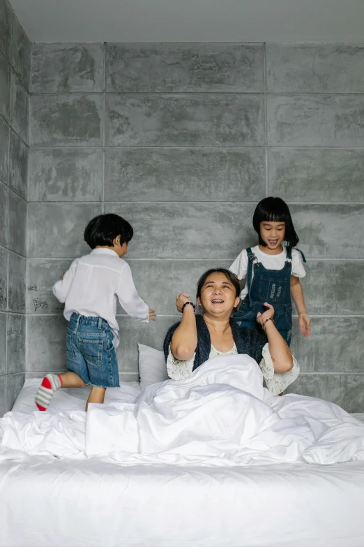 a woman sitting on top of a bed next to two children, by Basuki Abdullah, pexels contest winner, conceptual art, laughing, kim hyun joo, in an action pose, white sheets