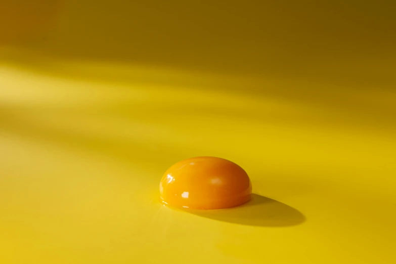 an egg laying on top of a yellow surface, by Doug Ohlson, jelly, light orange mist, smooth waxy skin, mid shot