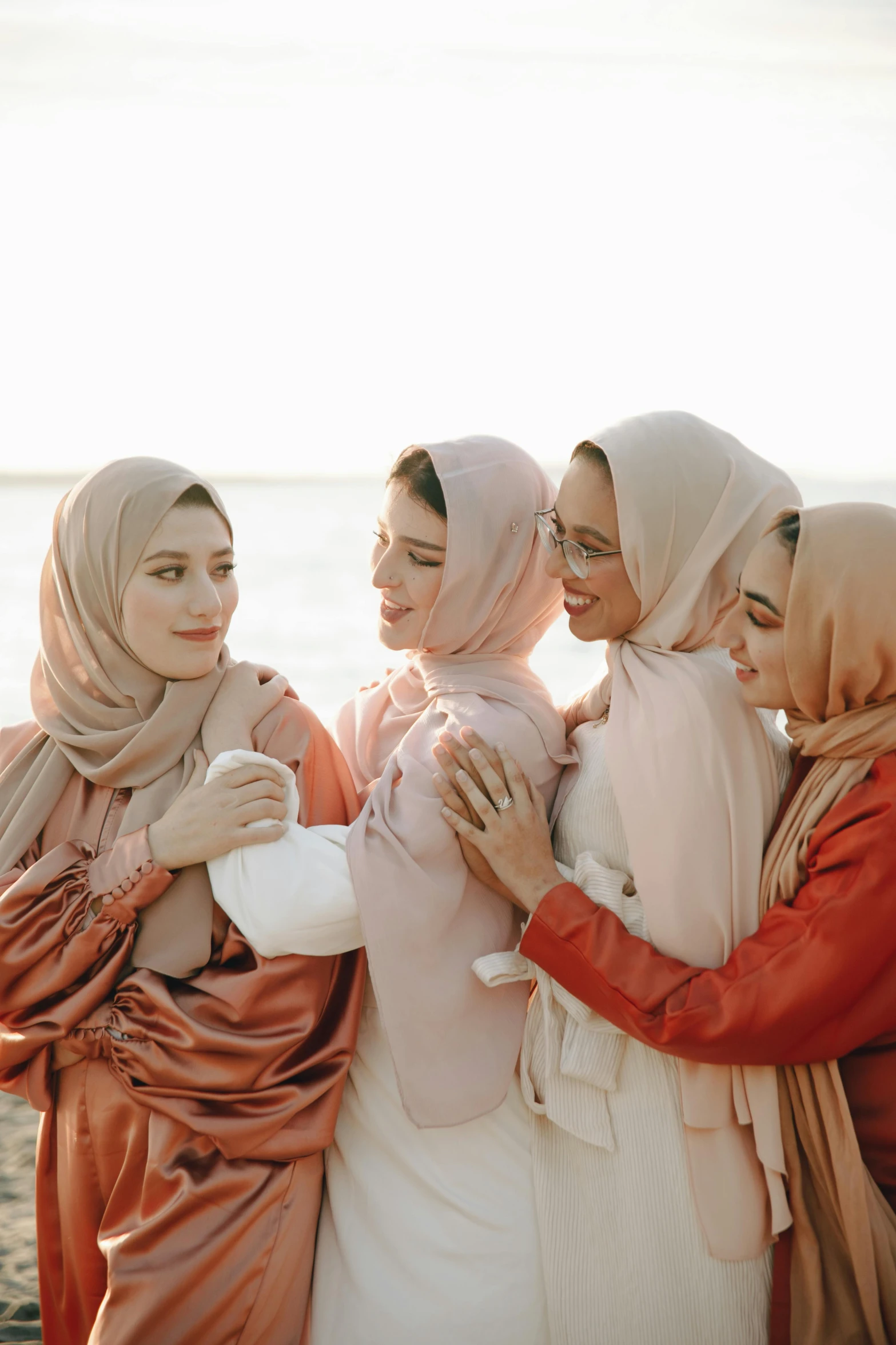 a group of women standing next to each other on a beach, a picture, inspired by Maryam Hashemi, trending on pexels, hurufiyya, wearing a scarf, soft red tone colors, photoshoot for skincare brand, white hijab