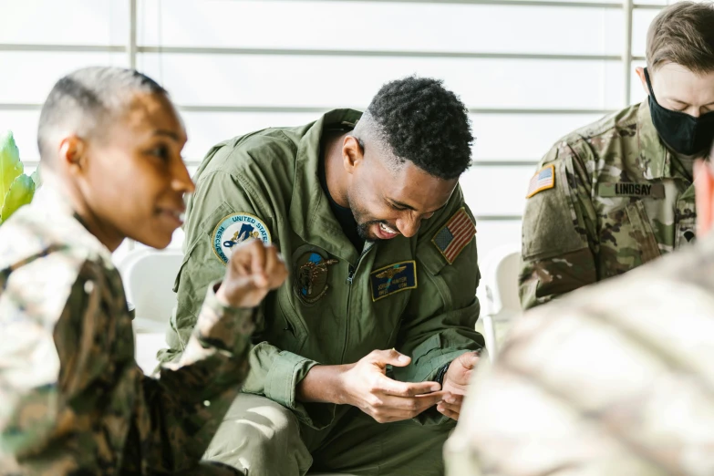 a group of men sitting around each other looking at a cell phone, air force jumpsuit, profile image, jemal shabazz, supportive