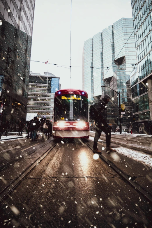 a red bus driving down a street next to tall buildings, pexels contest winner, snow flurry, toronto city, people, street tram