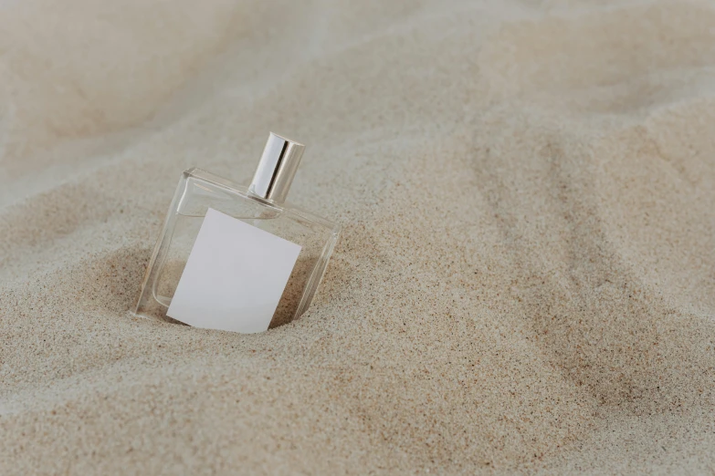 a bottle of perfume sitting in the sand, inspired by Nicolas de Staël, unsplash, silver，ivory, paper, rectangle, coastal