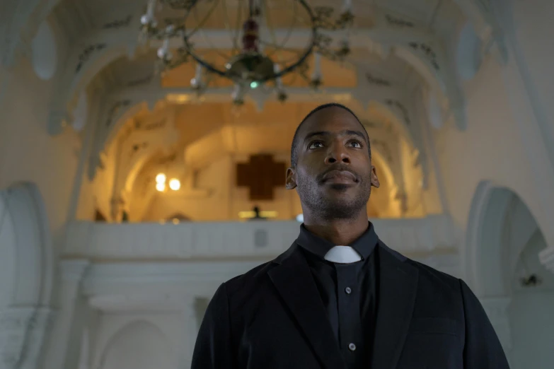 a man in a suit standing in front of a chandelier, pexels contest winner, happening, scene set in a church, black man, in black uniform, promotional image