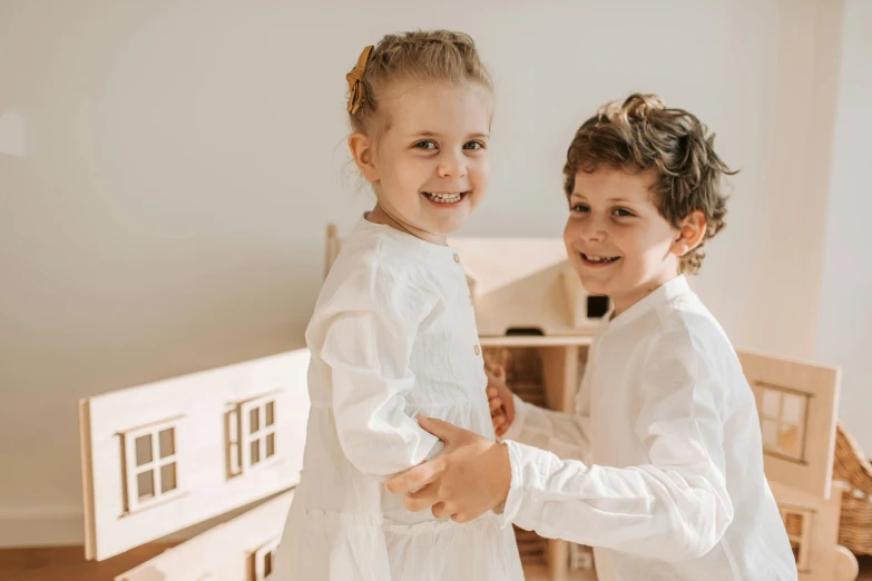 a couple of kids standing next to each other, by Emma Andijewska, pexels contest winner, arts and crafts movement, french provincial furniture, wearing white pajamas, activity play centre, mini model