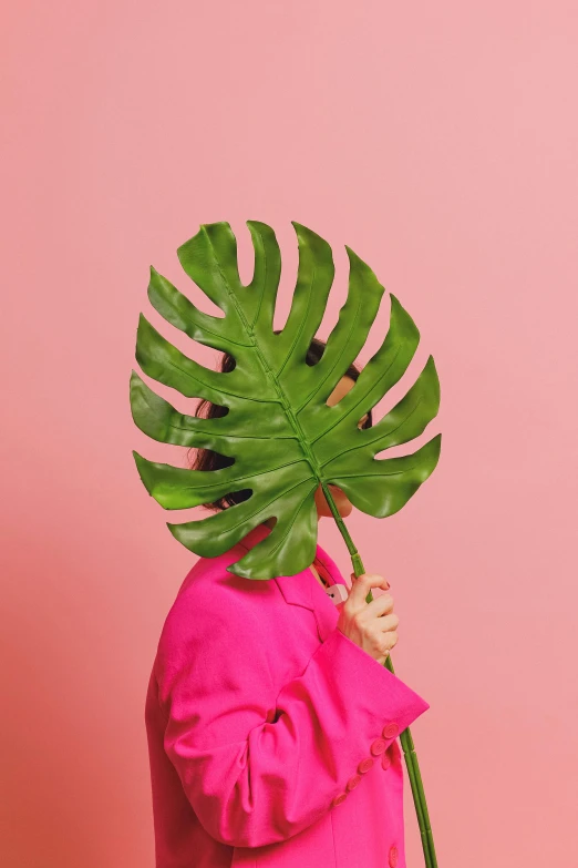 a woman holding a large green leaf over her head, an album cover, inspired by Ren Hang, trending on pexels, hot pink, helmet instead of a head, close - up studio photo, hiding behind obstacles