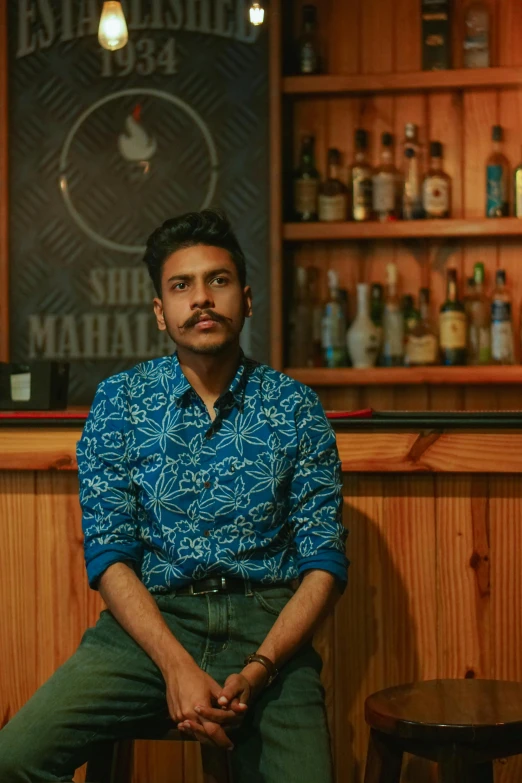 a man sitting on a stool in front of a bar, jayison devadas, profile image, frontal pose, looking serious
