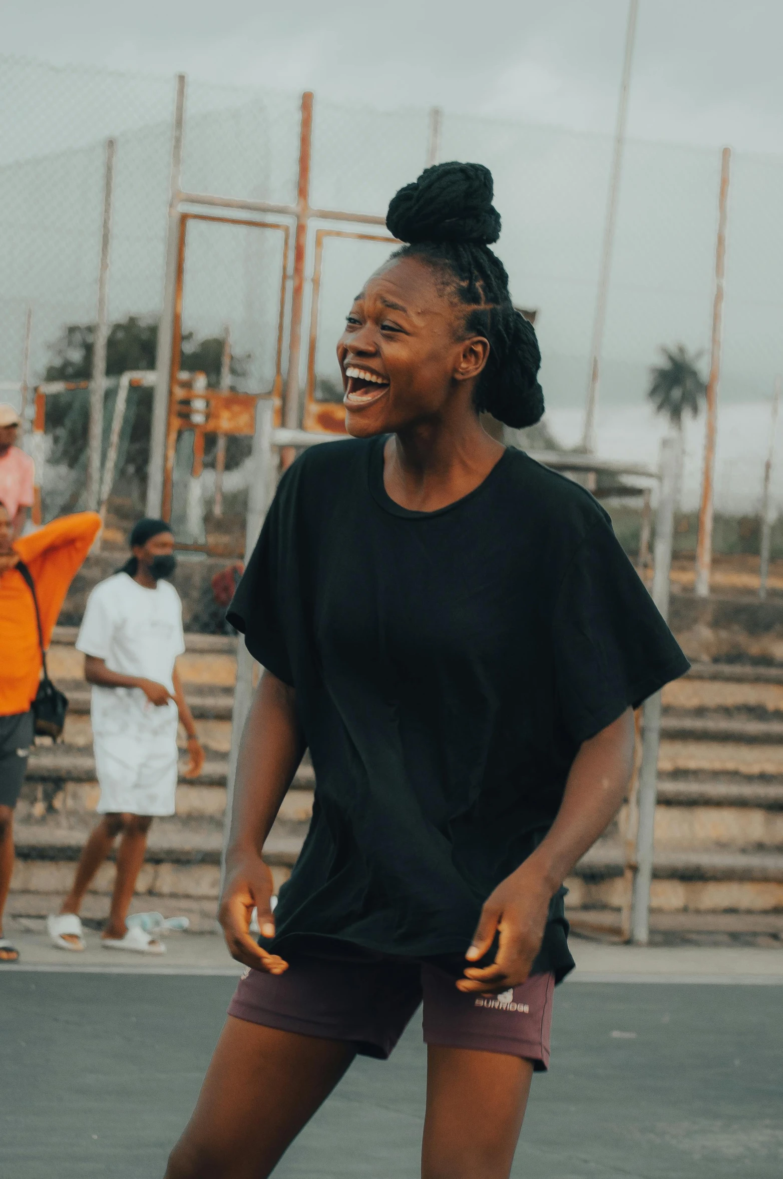 a woman standing on top of a tennis court holding a racquet, an album cover, by Chinwe Chukwuogo-Roy, pexels contest winner, happening, earing a shirt laughing, wearing a black tshirt, people walking around, trending on vsco