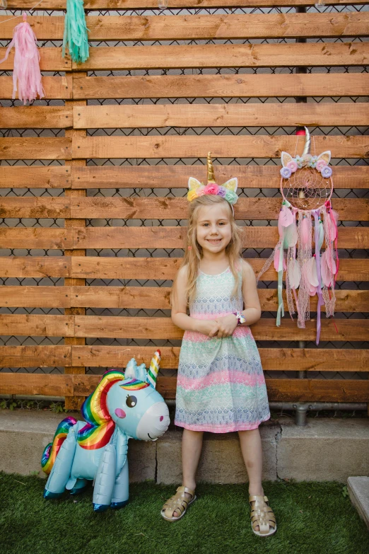 a little girl standing in front of a wooden fence, unicorns, fully decorated, posing for a picture, profile image