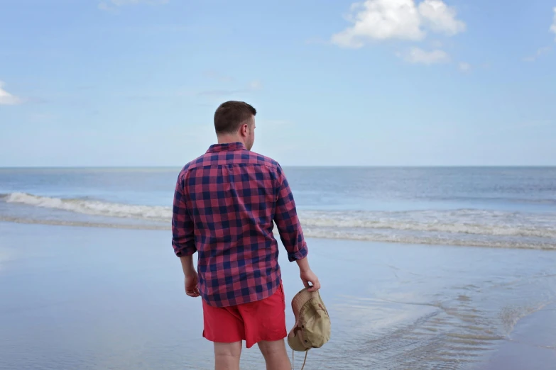 a man standing on top of a beach next to the ocean, wearing a red lumberjack shirt, indigo and venetian red, wearing red shorts, profile image