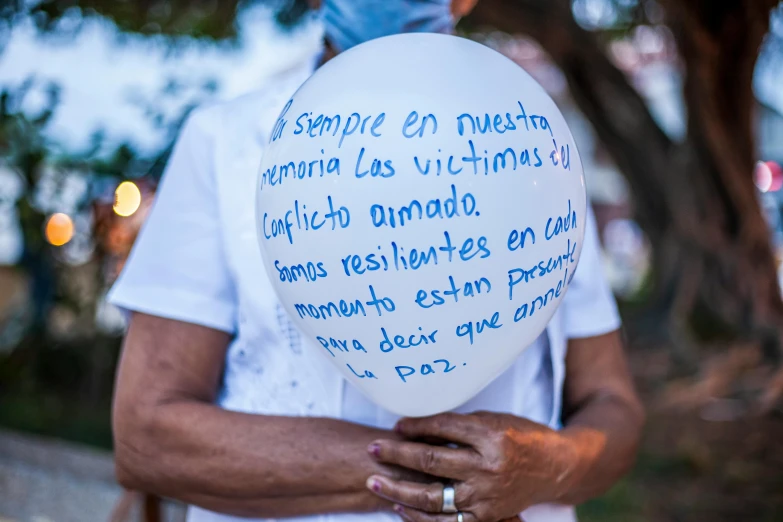 a person holding a balloon with writing on it, by Gina Pellón, white ribbon, mexico, puerto rico, tragedy