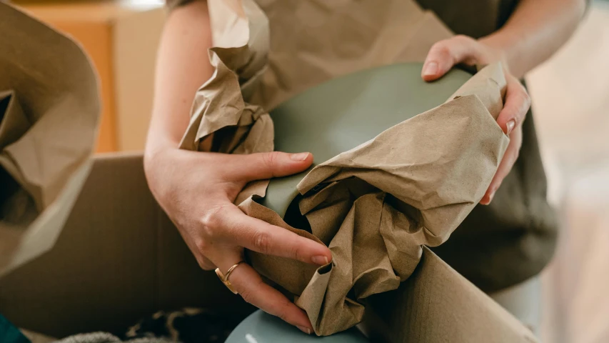 a woman wrapping a gift wrapped in brown paper, inspired by Sarah Lucas, pexels contest winner, arts and crafts movement, muted green, sydney hanson, soft vinyl, curved furniture