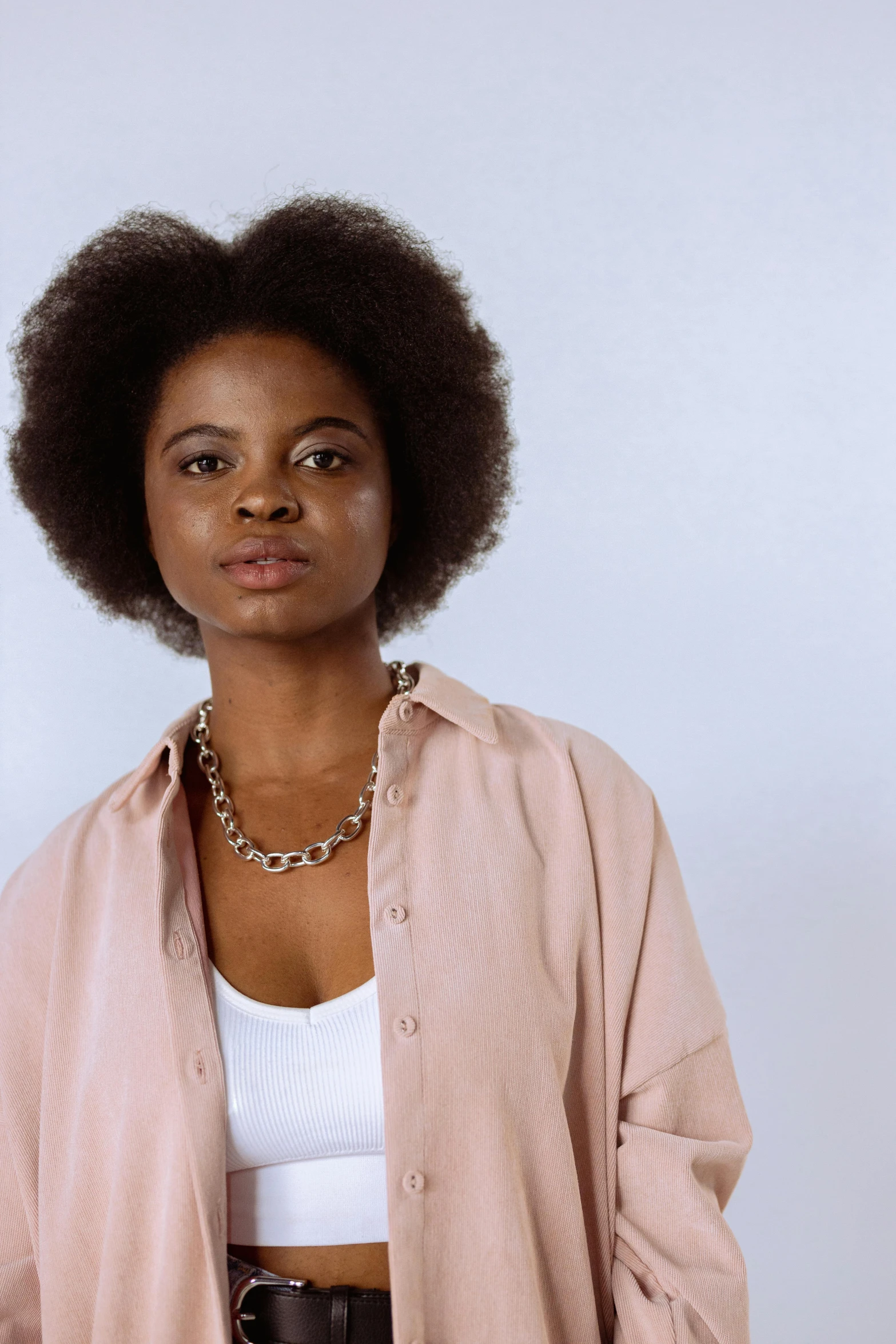 a woman with an afro is posing for a picture, by Lily Delissa Joseph, wearing a light shirt, wearing a chain, plain background, lena oxton