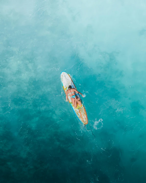 a person riding a surfboard on top of a body of water, looking down from above