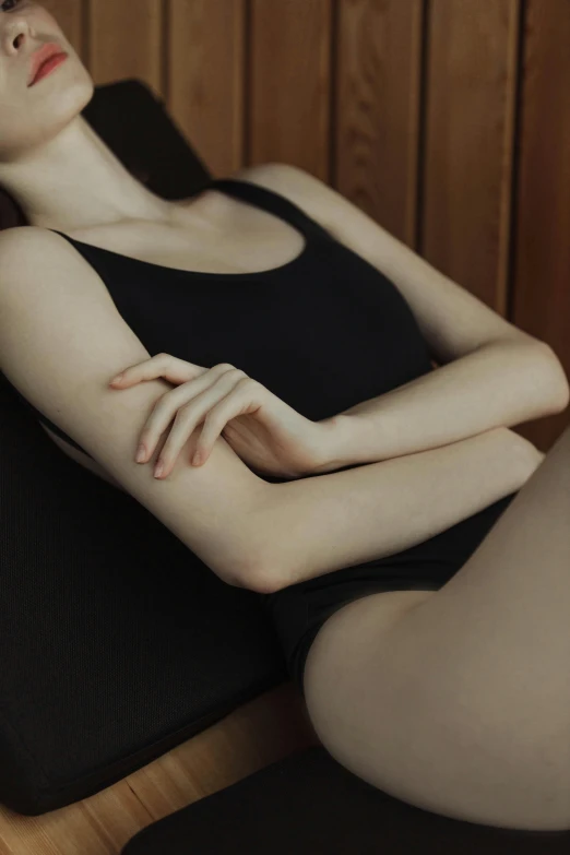 a woman that is laying down in a chair, inspired by Vanessa Beecroft, unsplash, aestheticism, closeup of arms, black swimsuit, soft flawless pale skin, wearing a cropped black tank top