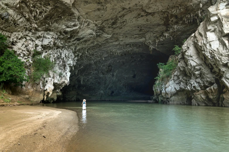 a man standing in the water in front of a cave, by Jan Kupecký, pexels contest winner, minimalism, laos, white, lush surroundings, kent monkman