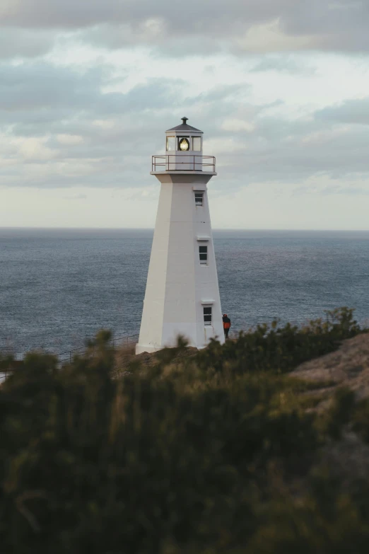 a white lighthouse sitting on top of a cliff next to the ocean, ignant, brightly-lit, no crop, college