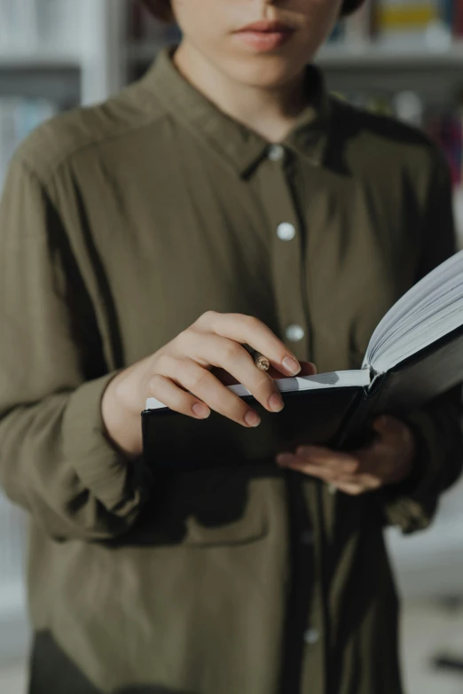 a woman reading a book in a library, an album cover, by Carey Morris, trending on unsplash, wearing a black shirt, zoomed in, he is holding a large book, office clothes