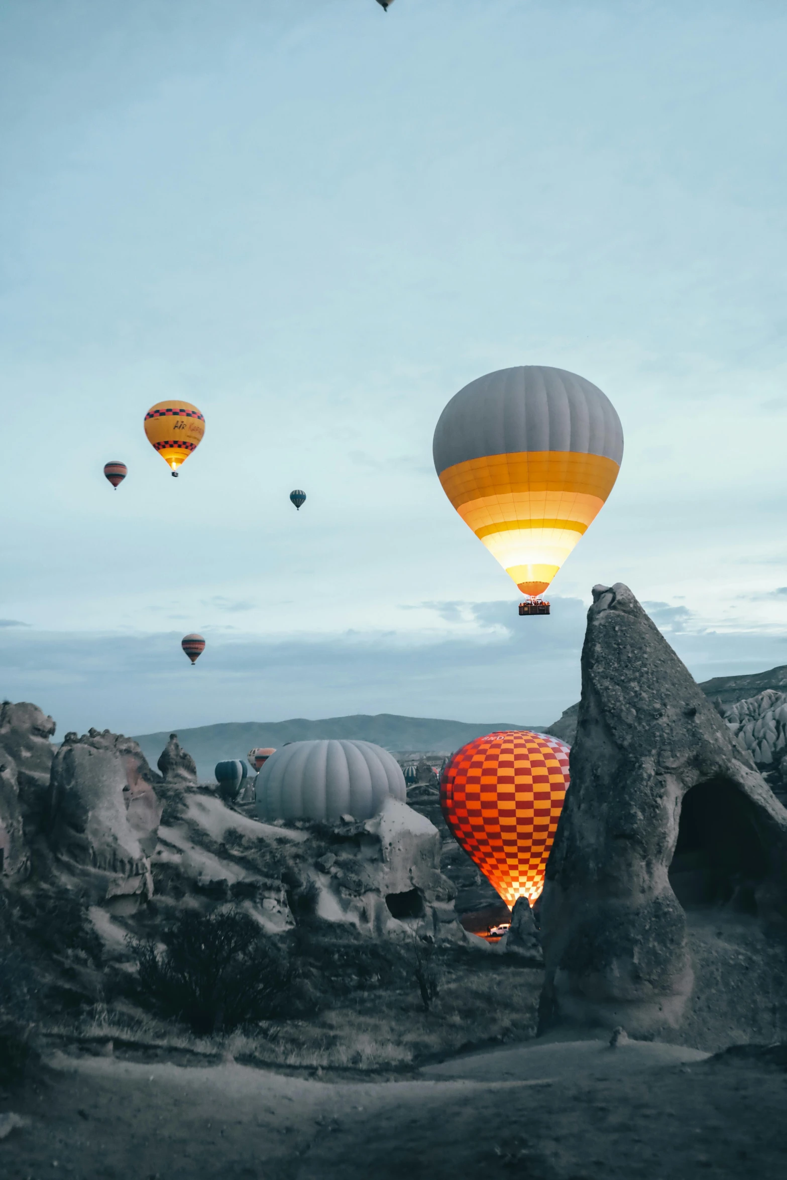 a group of hot air balloons flying over a rocky landscape, by irakli nadar, pexels contest winner, yellow lanterns, helicopter view, helmet is off, dusk setting