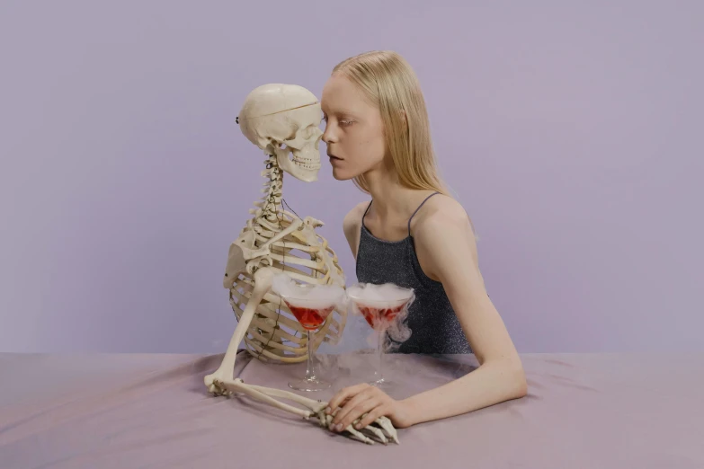 a woman sitting at a table with a skeleton in front of her, an album cover, inspired by Sarah Lucas, tumblr, aestheticism, drinking cocktail, albino white pale skin, ignant, petra collins