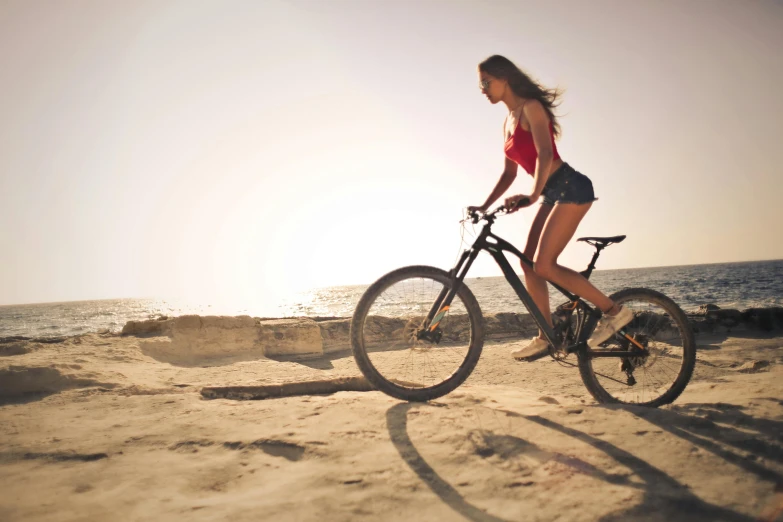 a woman riding a bike on top of a sandy beach, wearing a tank top and shorts, trending on, action sports, soft cracks